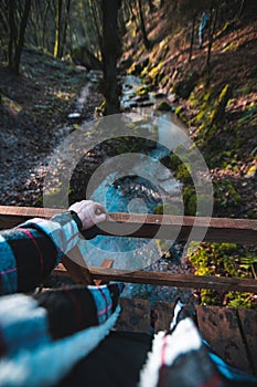 Man standing on a wooden Bridge looking down a small stream