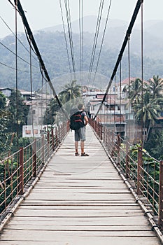 Man standing on wooden suspension bridge in a mountain village of Laos