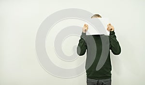 Man is standingman in a green jumper is standing and holding a blank sheet