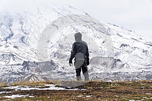 A man stands alone against the backdrop of a large mountain. Bad weather