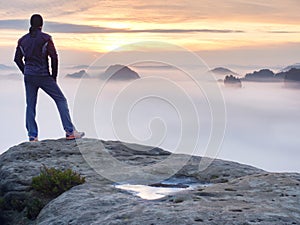 Man stands alone on the peak of rock. Hiker watching to autumn Sun at horizon