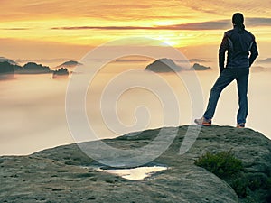 Man stands alone on the peak of rock. Hiker watching to autumn Sun at horizon