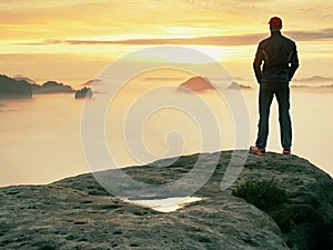 Man stands alone on the peak of rock. Hiker watching to autumn Sun at horizon . Beautiful moment the miracle of nature