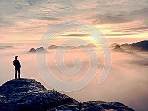 Man stands alone on the peak of rock. Hiker watching to autumn Sun at horizon