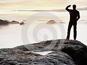 Man stands alone on the peak of rock. Hiker watching to autumn Sun at horizon .