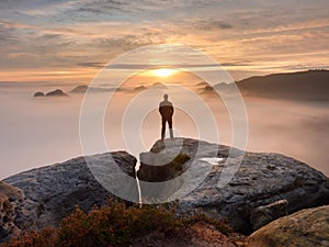 Man stands alone on the peak of rock. Hiker watching to autumn Sun at horizon