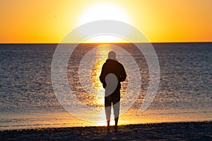 Man stands on the beach next to surf, admires amazing sunset