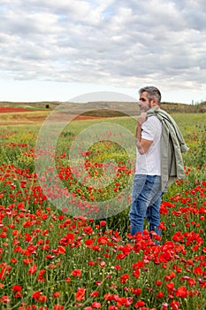 A man stands in a blooming poppy field and looks into the distance.