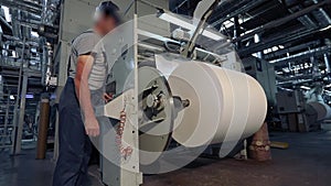 A man stands in a factory for the production of wallpaper. A man at the factory controls the machine