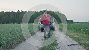 man stands in field near broken minivan car sadly talking on phone