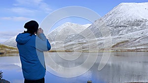 A man stands on a high point in the mountains and admires a beautiful view. There are peaks around it and a beautiful