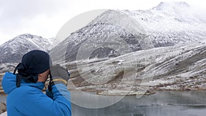 A man stands on a high point in the mountains and admires a beautiful view. There are peaks around it and a beautiful