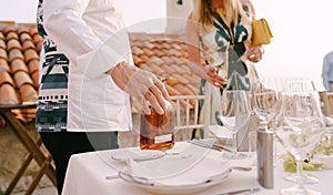 Man stands near a served table and holds a bottle of alcohol with his hand against a background of a woman with an empty