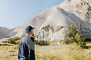 The man stands next to the beautiful rocks and admires the scenery in Cappadocia in Turkey. The landscape of Cappadocia