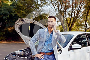 Man stands next to a broken car calling