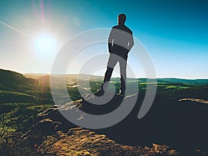 Man stands on the peak of sandstone rock watching over valley to Sun. Beautiful moment