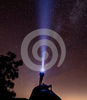 A man stands on a rock with a headlamp while another rests