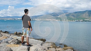 Man stands on rocks on background of floating people. Concept. Man stands by water with floating vacationers on sea. Man