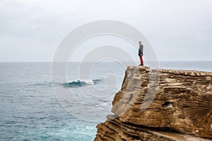 Man stands on a sea cliff, looking into the distance on a dark stormy sea.