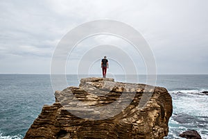 Man stands on a sea cliff, looking into the distance on a dark stormy sea.