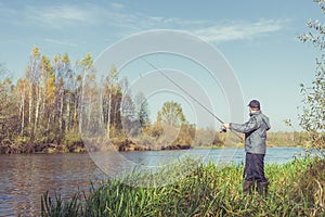 Man stands on the shore with a fishing rod. Angler in a jacket with a fishing rod stands on the river bank