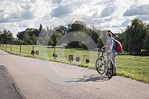 Man stands at the side of a country lane road with bicycle looking at sheep