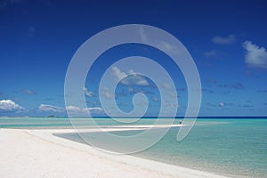A man stands at the tip of a white sandy beach surrounded by a turquoise lagoon on the island of Fakarava, French Polynesia in the photo