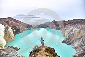 The man stands on top of the volcano and looks at the lake in the crater.