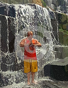 Man stands under a waterfall with his hands folded across his chest in prayer
