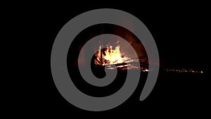 A man stands and watches at a broken down burning bonfire at night time in slow motion