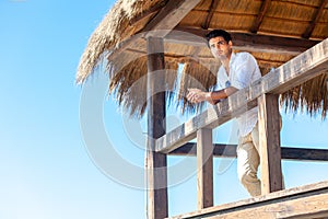Man stands on wooden hut bungalow at the beach by the sea