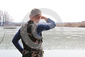The man stares into the distance while standing on the shore of the lake.