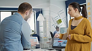 Man in startup office zoomin in digital tablet using touchscreen presenting sales charts to woman colleague