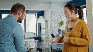 Man in startup office zoomin in digital tablet using touchscreen presenting sales charts to woman colleague