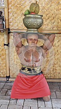 Man statue or mannequin in the restaurant corner kneel with hands up at the back and fruit pot above the head, used as a artistic