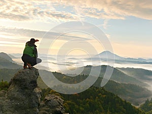 Man stay on rocky peak within daybreak and watch over misty landscape.