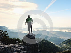 Man stay on rocky peak within daybreak and watch over misty landscape.