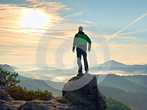 Man stay on rocky peak within daybreak and watch over misty landscape.