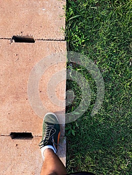 Man step up on right foot in green sneaker. cement drain grate and green grass with abstract background