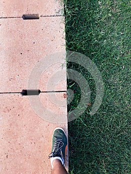 Man step up on right foot in green sneaker. cement drain grate and green grass with abstract background