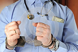 Man with stethoscope holds his hands in handcuffs before itself