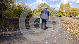 Man with stick walking lonely with old green suitcase on a country road and turn left