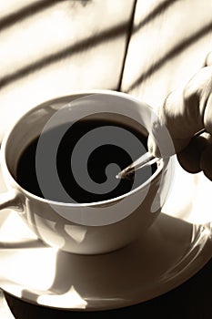 Man stiring a cup of black coffee in sunlight on a wooden table