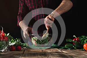 Man stirring salad of fresh vegetables on wooden table