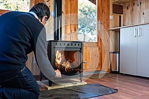 Man stoking the fire in a rustic cast iron fireplace to heat the house in winter