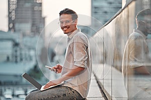 Man on the street. Attractive man sitting outside, using mobile phone and laptop, smiling