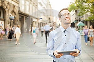 Man on street looking up, hold tablet in hands