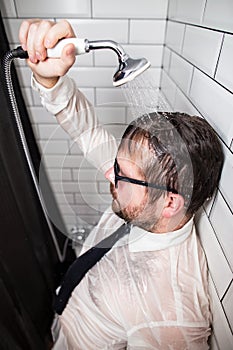 Man in stress after work. He stands in the bathroom in glasses and clothes, pouring running water over himself from a