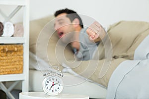 man stretching in bed alarmclock in foreground