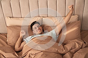 Man stretching in bed with brown linens at home